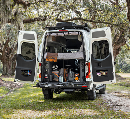 A Mercedes-Benz Cargo Van parked with the rear doors open showcasing the camper van cargo space.