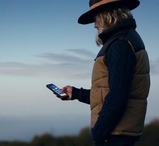 A person standing outdoors holding a phone and using the Mercedes me connect app for their Mercedes-Benz Adventure van. 