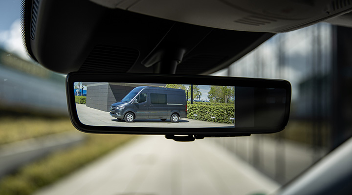 A driver inside the Mercedes-Benz Sprinter Van looking into the digital rear-view mirror. 